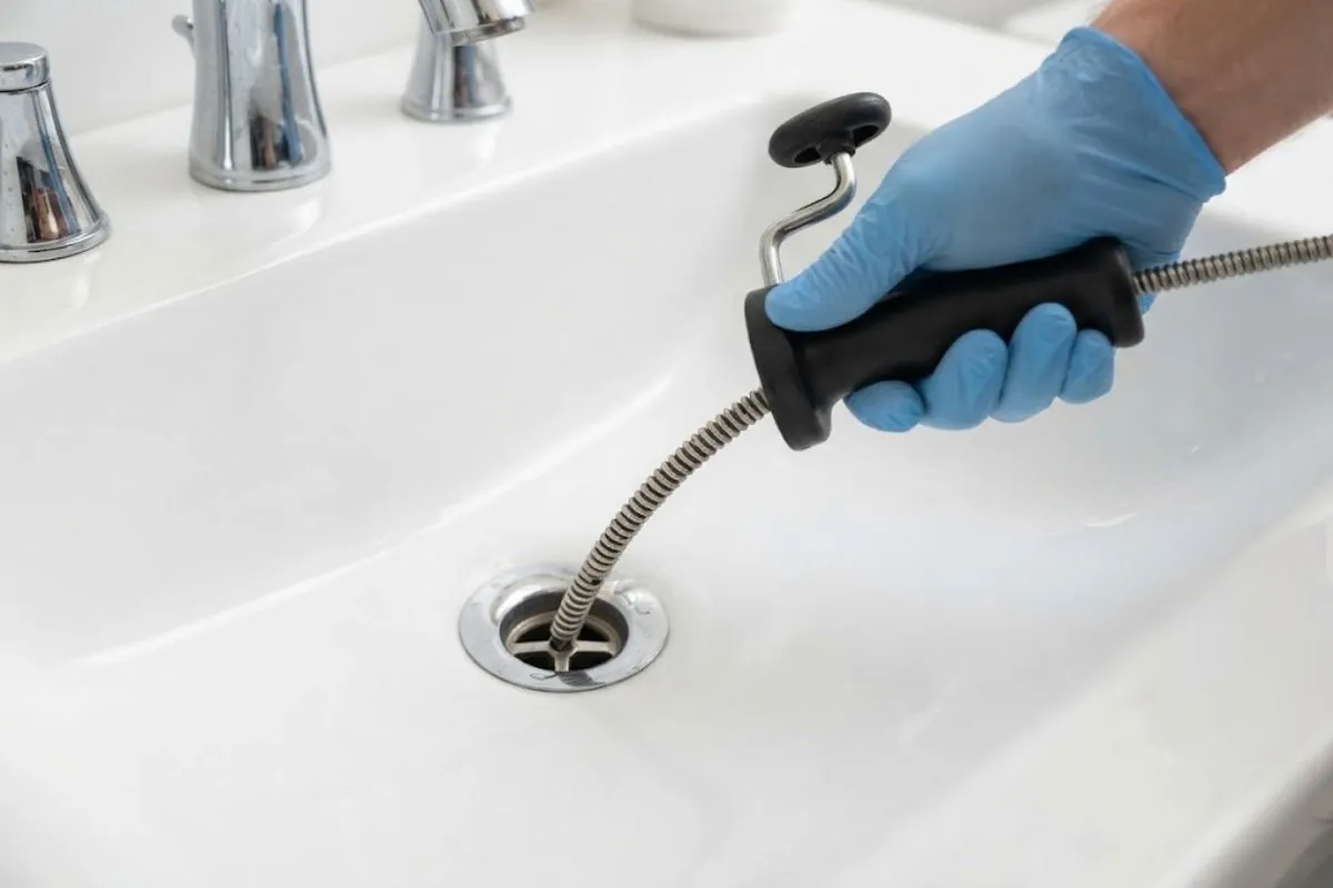 Hand-held drain auger entering a bathroom sink drain