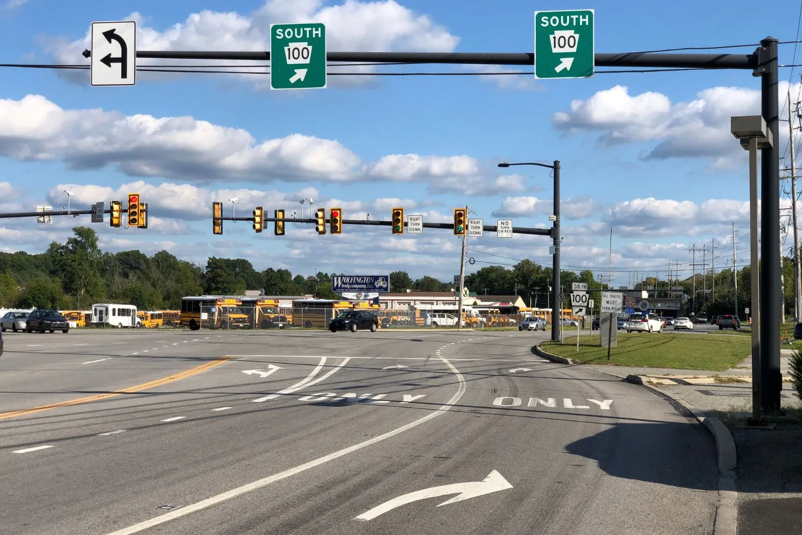 Intersection with overhead Route 100 South signs and school buses in the distance