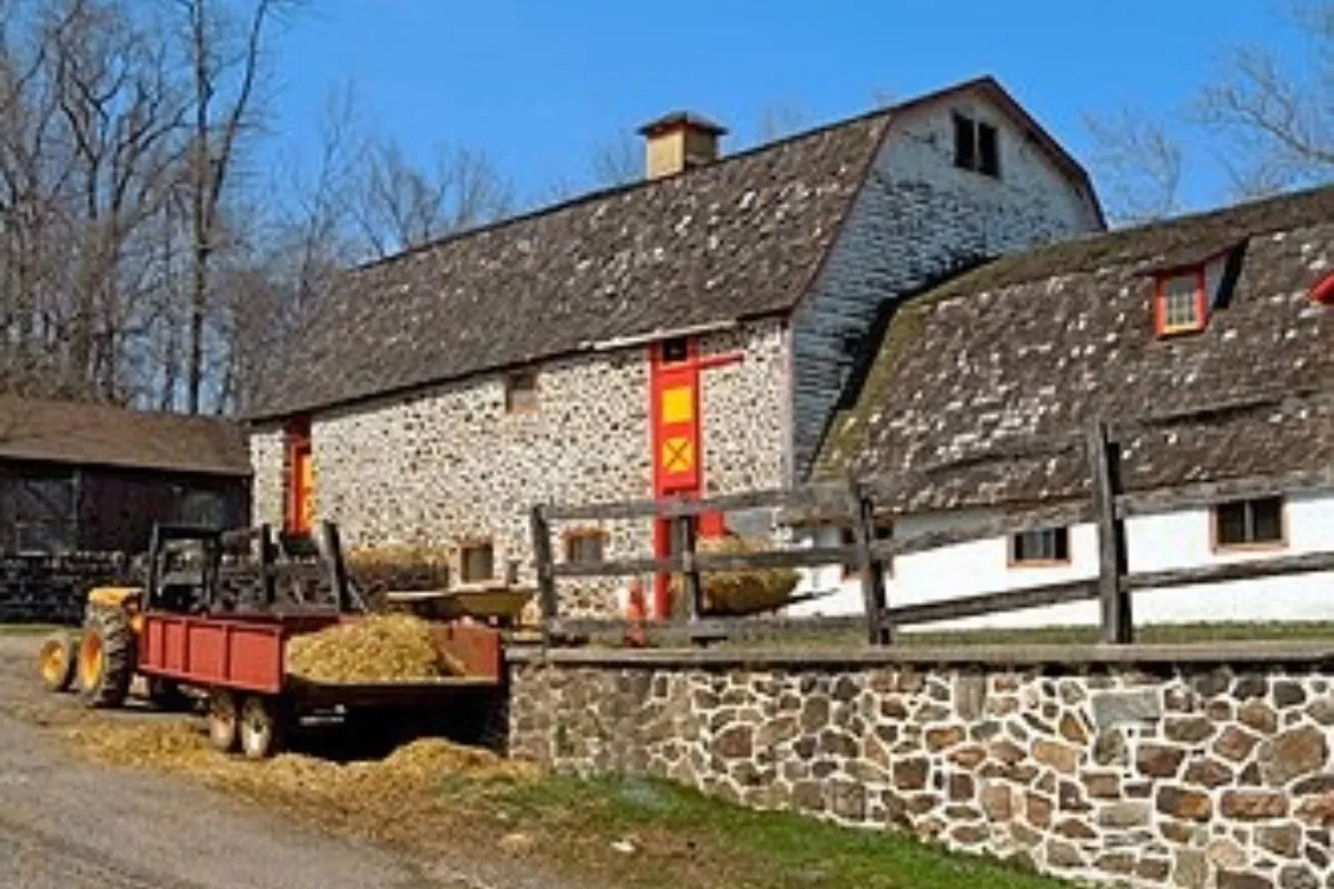 Stone barn with a tractor and trailer beside a stone wall