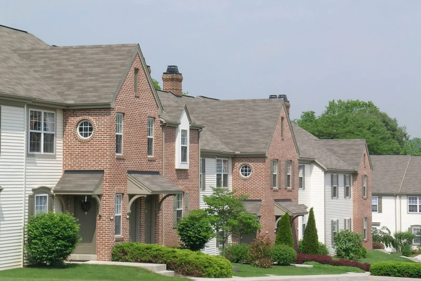 Brick townhouses with gabled roofs and landscaped shrubs