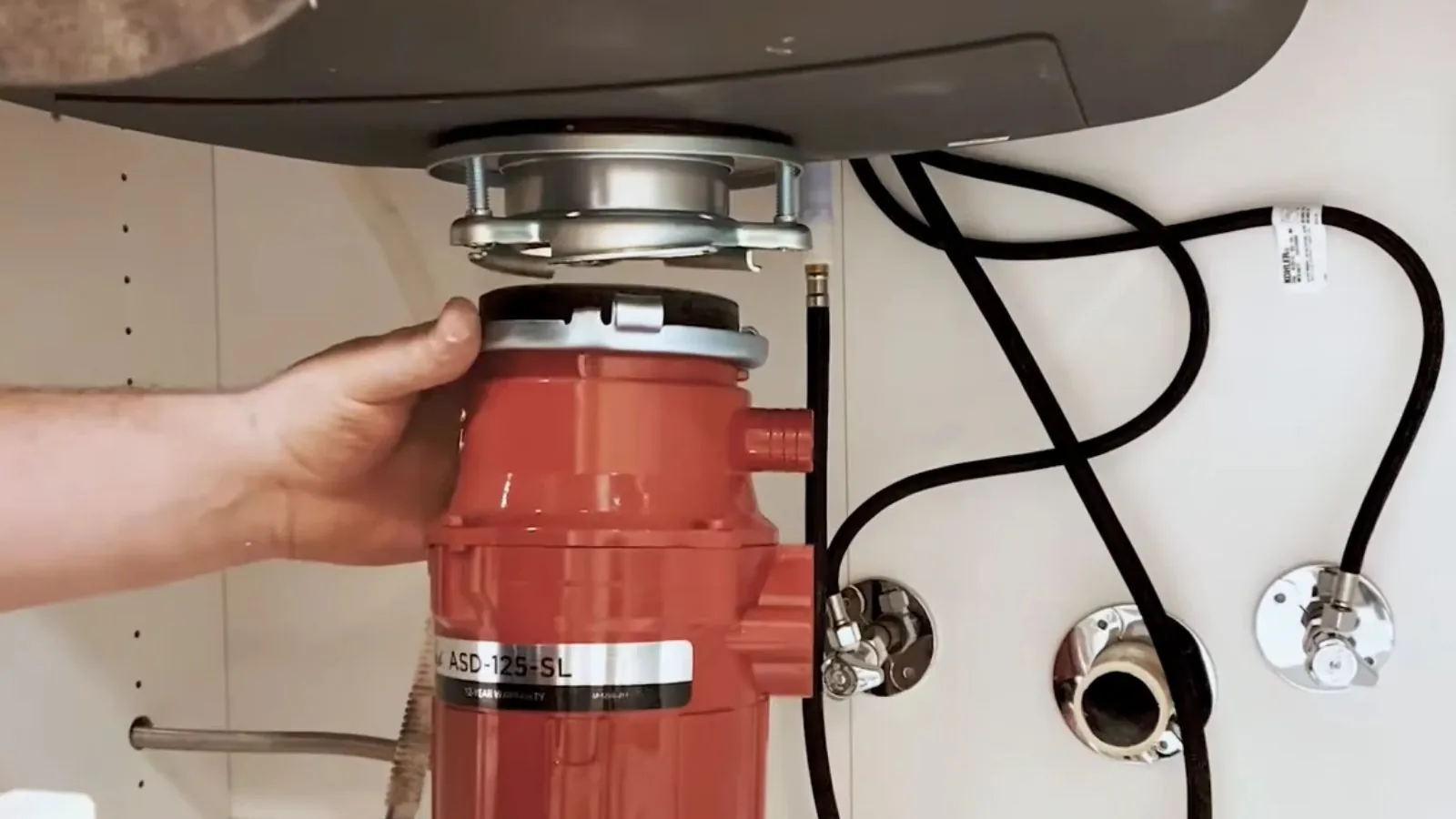 Hand holding a red garbage disposal unit under a kitchen sink