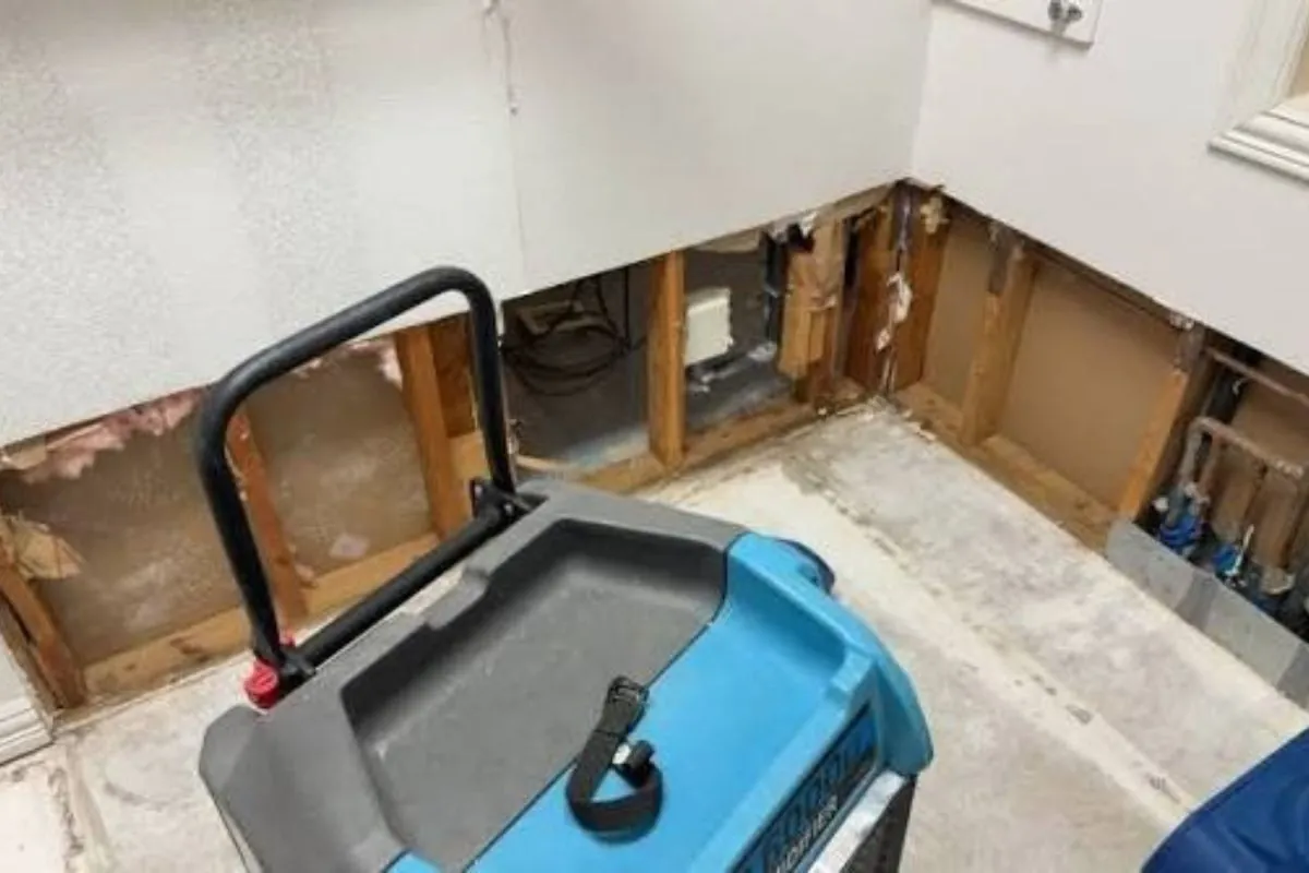 Dehumidifier in a basement with a section of wall cut open to dry