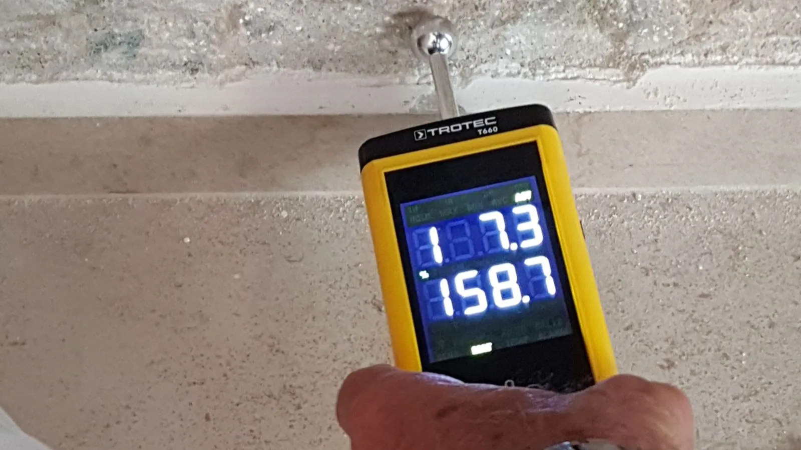 Hand holding a moisture meter against a concrete block wall